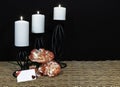 Beautiful orange and white roses, white candle perched on black candle holders on mesh place mat and wooden table with card and da