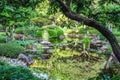 Beautiful oriental garden with tiny cement temple and pond with reflection of trees and lily pads - selective focus Royalty Free Stock Photo