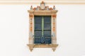 Beautiful ornate window with decorative trim with yellow and blue design elements in a white plaster wall of an old building