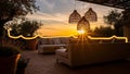 Beautiful outdoor patio setting features comfortable modern sofas illuminated by glowing string lights against a vivid sunset Royalty Free Stock Photo