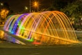 Beautiful outdoor view of colorful water entertainment structure fountain, at long exposure in the night, with buildings Royalty Free Stock Photo