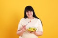 Beautiful overweight woman eating salad on yellow background. Healthy diet Royalty Free Stock Photo