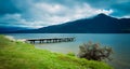 Beautiful panorama of a pier on Kaniere Lake with the green mountain in the background on a cloudy day, New Zealand
