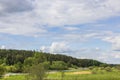 Beautiful panoramic view of forest trees on mountain and river flowing along fields on backdrop of blue sky with white clouds. Royalty Free Stock Photo