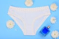 Beautiful panties with bottle of perfume and flower buds on blue background. Women underwear set. Romantic lingerie.