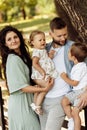 Beautiful parents with little kids at the park, loving dad hold in arms adorable daughter and lovely son, happy mom hold Royalty Free Stock Photo