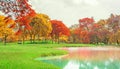 A beautiful park in an autumn season, yellow and orange colorful leaves of the trees on green grass fresh lawn near a lake Royalty Free Stock Photo