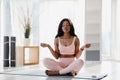 Beautiful peaceful young black woman sitting in lotus pose, meditating with closed eyes, practicing yoga on mat at home Royalty Free Stock Photo