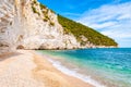 Beautiful pebble beach surrounded by high massive white limestone rocky cliffs eroded by Adriatic sea waves and wind. Green Aleppo Royalty Free Stock Photo