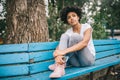 Beautiful pensive African American woman sitting on bench outdoors in the park. Pretty dark-skinned female sitting in the park Royalty Free Stock Photo