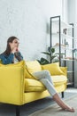 beautiful pensive barefoot girl sitting on sofa and looking away