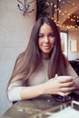 Beautiful pensive happy girl sitting in cafe in Christmas holidays, smiling and dreaming. Brunette woman with long hair drinks