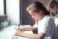 Beautiful pensive teenager girl drawing sketch at her table with light from window in home Royalty Free Stock Photo