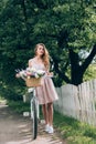 beautiful pensive woman in dress with retro bicycle with wicker basket full of flowers