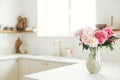 Beautiful peonies in vase on granite countertop on background of stylish white kitchen with wooden shelves and appliances in new Royalty Free Stock Photo