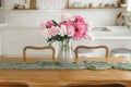 Beautiful peonies in vase on wooden table on background of stylish white kitchen with appliances in new rustic farmhouse. Modern Royalty Free Stock Photo