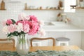 Beautiful peonies in vase on wooden table on background of stylish white kitchen with appliances in new scandinavian house. Royalty Free Stock Photo