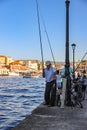 Beautiful photo of old man fishing in harbor with other fishermen in background.