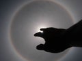 Beautiful photograph of the sun with a circular rainbow surrounded by a bright sky and white clouds with shadows of hands reaching