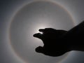 Beautiful photograph of the sun with a circular rainbow surrounded by a bright sky and white clouds with shadows of hands reaching