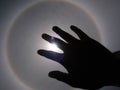 Beautiful photograph of the sun with a circular rainbow surrounded by a bright sky and white clouds with shadows of hands reaching Royalty Free Stock Photo