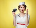 Beautiful pin-up girl dressed a sailor holding a vintage camera and screams behind his hand. Yellow background, close up