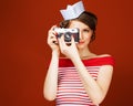 Beautiful pin-up girl holding a vintage camera and directs it straight to the camera. Red background, close up