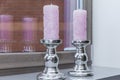 Beautiful pink candles in silver candlesticks on the window. Close-up. Comfort and holiday in the house