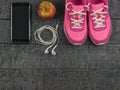 Beautiful pink sneakers, headphones, water and apples on a wooden black floor. View from above. Royalty Free Stock Photo