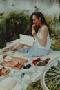 Beautiful playful woman is reading book and eating croissant at picnic Royalty Free Stock Photo