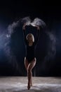 Beautiful plump blonde girl wearing a black gymnastic bodysuit covered with clouds of the flying white powder jumps dancing Royalty Free Stock Photo