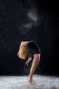 Beautiful plump blonde girl wearing a black gymnastic bodysuit covered with clouds of the flying white powder jumps dancing Royalty Free Stock Photo