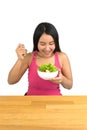 Beautiful plus size Asian woman sitting at the wooden table and holding a bowl of salad