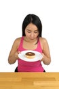 Beautiful plus size Asian woman sitting at the wooden table and holding a plate with doughnut