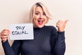 Beautiful plus size woman asking for equality economy holding paper with pay equal message pointing thumb up to the side smiling