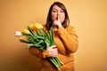 Beautiful plus size woman holding romantic bouquet of natural tulips flowers over yellow background asking to be quiet with finger Royalty Free Stock Photo