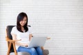 Beautiful of portrait asian young woman working online laptop sitting on chair on cement brick white background Royalty Free Stock Photo