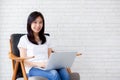 Beautiful of portrait asian young woman working online laptop sitting on chair on cement brick white background Royalty Free Stock Photo