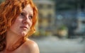 Beautiful portrait in closeup of a young elegant red-haired curly woman by the sea at the fishing village in Italy with copy space Royalty Free Stock Photo