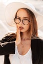 Beautiful portrait pretty young gorgeous woman with sexy lips in youth glasses in black jacket in elegant hat on bright sunny day Royalty Free Stock Photo