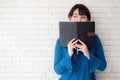 Beautiful portrait young asian woman happy hiding behind covering the book with cement or brick concrete background Royalty Free Stock Photo