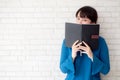 Beautiful portrait young asian woman happy hiding behind covering the book with cement or brick concrete background Royalty Free Stock Photo