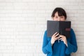 Beautiful portrait young asian woman happy hiding behind covering the book with cement or brick concrete background Royalty Free Stock Photo