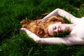 Beautiful Portrait of a young red-haired woman, raising her arms, lying in the summer sun on the green grass, the red hair Royalty Free Stock Photo