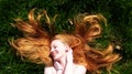 Beautiful portrait of a young sexy red-haired woman, lying in the summer sun in happiness, laughing, relaxing on the green grass, Royalty Free Stock Photo