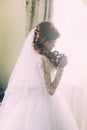 Beautiful portrait of young woman in white dress and veil at morning near window. Curly hairstyle