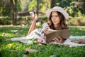 A beautiful and positive Asian woman is lying on a picnic mat and reading a book in a green park Royalty Free Stock Photo