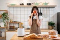 A beautiful, positive Asian woman is enjoying coffee in the kitchen while preparing her breakfast