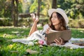 A beautiful and positive Asian woman is lying on a picnic mat and reading a book in a green park Royalty Free Stock Photo