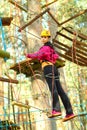 Beautiful positive brunette engaged climbing the trees. Girl in a special outfit goes on a suspension bridge.